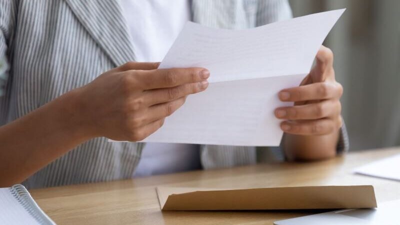 A person sitting at a desk reading a letter, with an opened envelope on the table