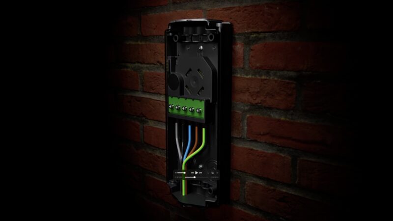 An opened wall-mounted EV charger unit on a brick wall with its internal wiring terminals and coloured cables exposed