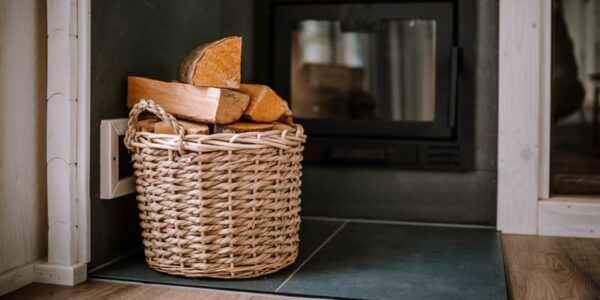 A wicker basket of firewood logs beside a black wood-burning stove
