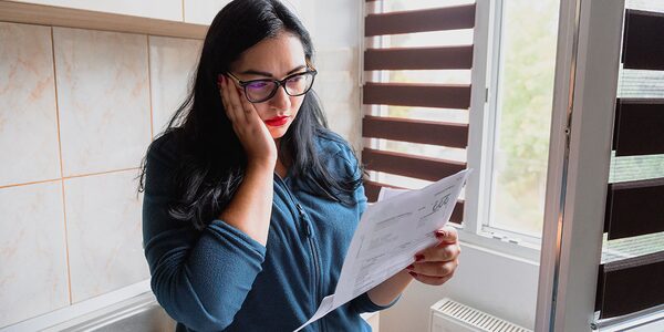 A woman with glasses looking concerned while reading a paper energy bill at home