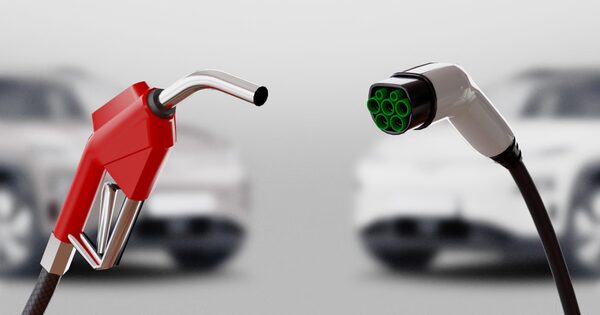 A red petrol pump nozzle and an EV charging plug facing each other in front of blurred cars