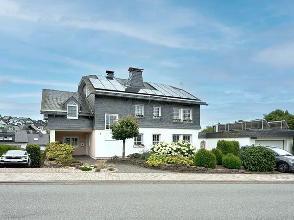 A large house with solar panels on its slate roof, seen from the street
