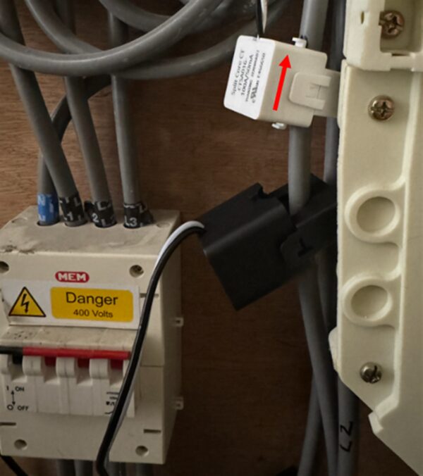 A CT clamp fitted around a cable inside a consumer unit next to an MEM 400V danger-labelled breaker