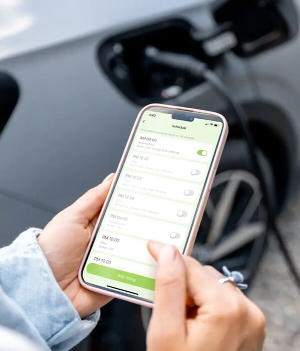 A person holding a smartphone showing the evec app charging schedule screen in front of an electric car plugged in at its charge port