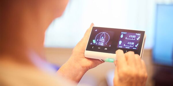A person holding and using a smart energy monitor displaying electricity usage and cost figures