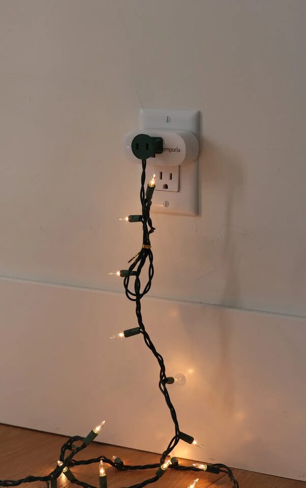 An Emporia smart plug in a wall socket powering a string of fairy lights