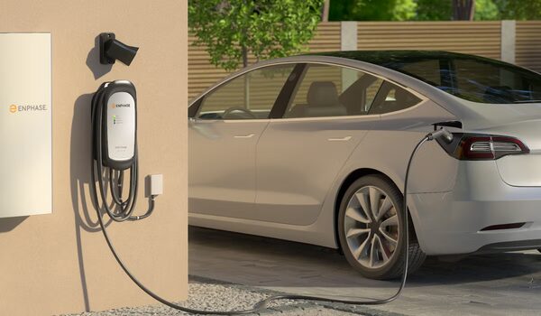 An Enphase wall-mounted EV charger charging a silver electric car outside a house