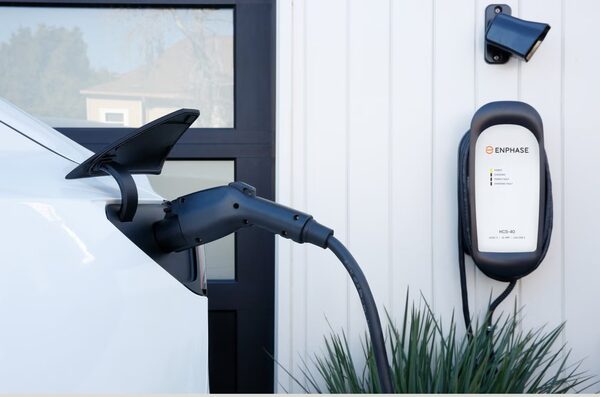 An Enphase HCS-40 wall-mounted EV charger plugged into a white car outside a house