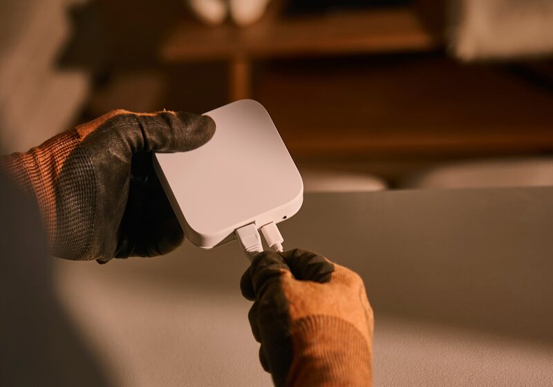 A gloved engineer's hands plugging cables into a white Hive smart hub device