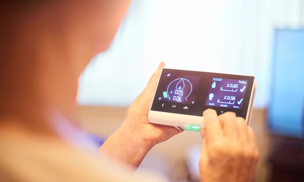 A person holding and using a smart energy display showing electricity usage and costs in pounds