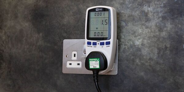 A plug-in energy monitor with digital display plugged into a UK wall socket