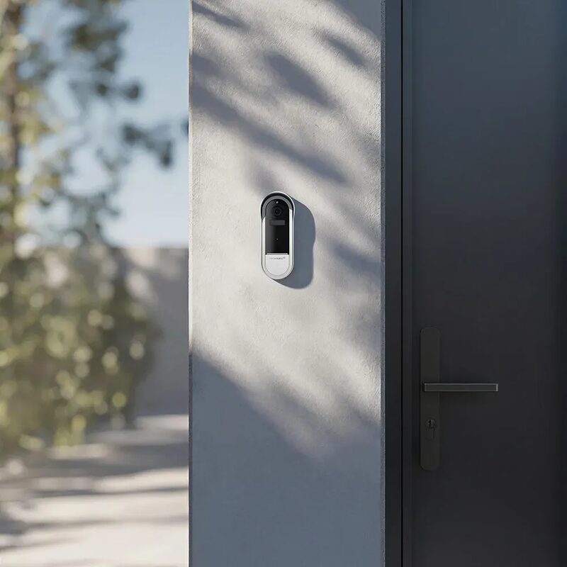 A Homematic IP video doorbell mounted on a wall beside a grey front door