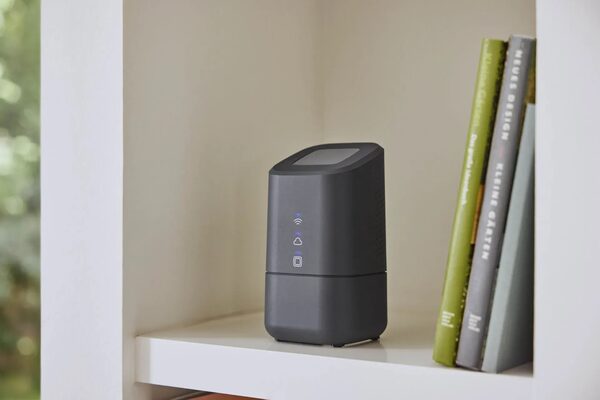 A dark grey Homematic IP smart home control unit with LED status lights sitting on a white shelf next to books