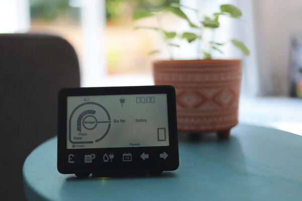 A smart energy monitor display showing a budget dial and energy usage, sitting on a blue table next to a potted plant