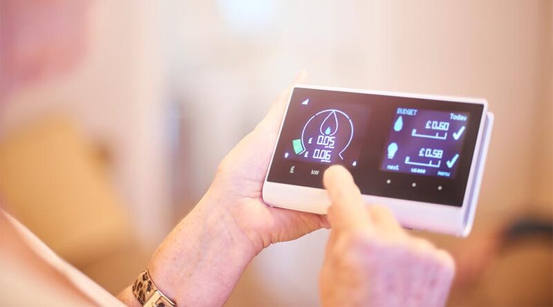A person touching a wall-mounted smart energy display showing water, electricity and gas usage with a daily budget in pounds