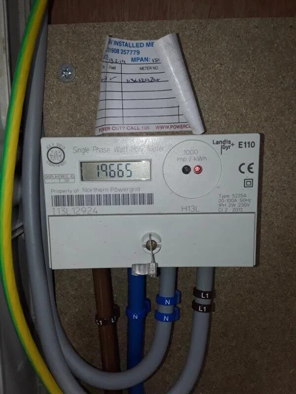 A Landis+Gyr E110 single-phase electricity meter installed on a wall with cabling and a paper MPAN label above it