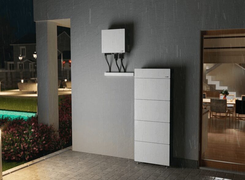 A tall white SolarEdge home battery and an inverter unit mounted on an exterior house wall at night in the rain