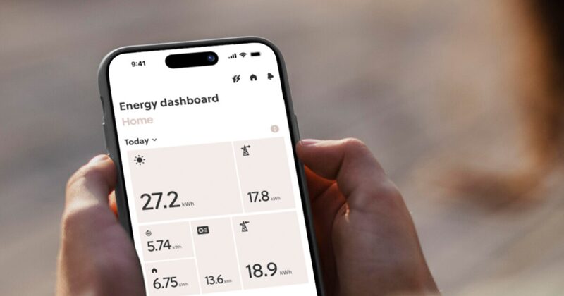 A hand holding a smartphone displaying the Smappee energy dashboard app with kWh usage figures