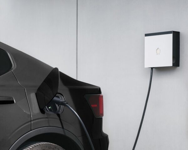 A Smappee wall-mounted EV charger on a grey wall with its cable plugged into a dark car