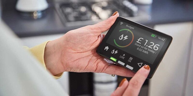 A person holding a smart meter display showing energy usage of £1.26 used so far today in a kitchen
