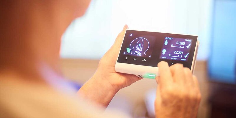 A person holding a smart meter in-home display showing energy usage and cost figures