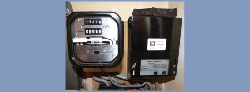 An old electricity meter and a Radio Teleswitch box mounted on a wall with wiring