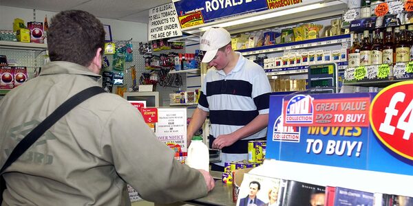 A customer topping up at the counter of a convenience shop with a shopkeeper behind the till