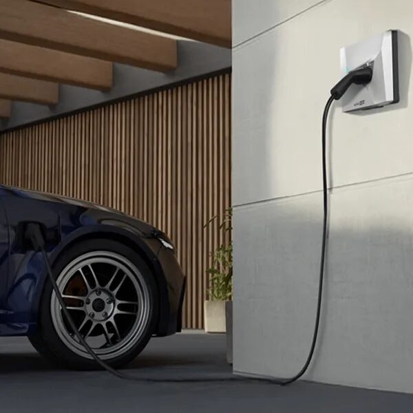 A SolarEdge wall-mounted EV charger with its cable plugged into a blue electric car parked in a modern carport