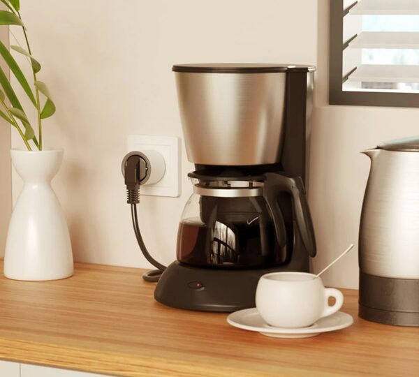 A smart plug in a wall socket powering a coffee maker on a kitchen worktop