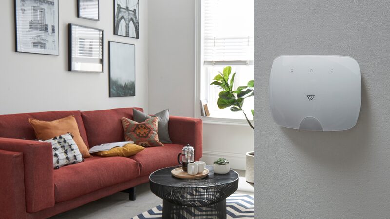A Wondrwall smart home control panel mounted on a wall beside a living room with a red sofa