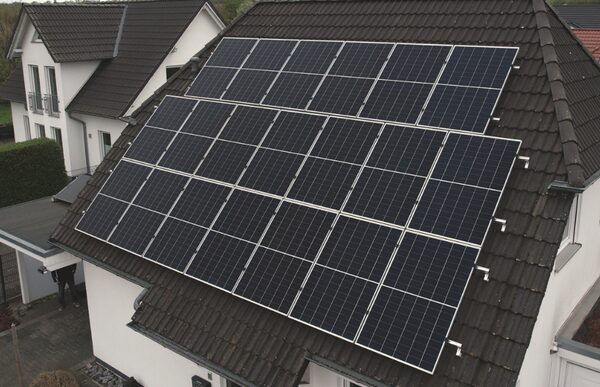 A large array of black solar panels mounted on the tiled roof of a white house