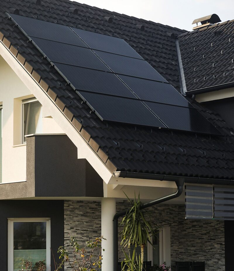 Black solar panels mounted on the tiled roof of a modern house