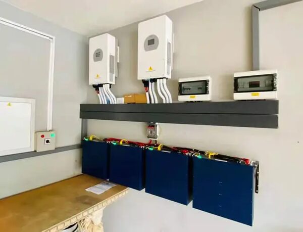 Two wall-mounted Deye hybrid inverters with consumer units and four blue lithium battery modules installed in a utility room