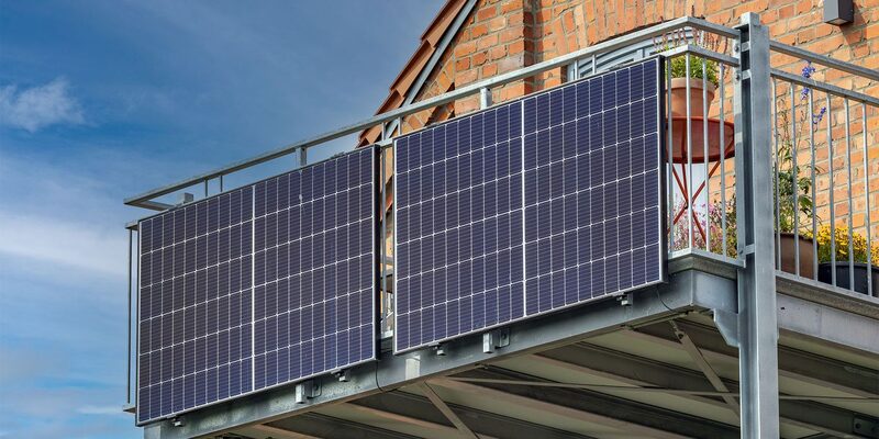 Two plug-in solar panels mounted on the railing of a brick house balcony
