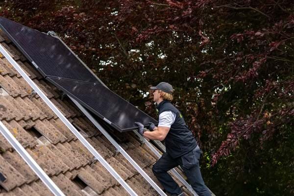 An installer lifting a solar panel onto mounting rails on a tiled pitched roof
