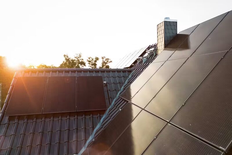 Black solar panels installed on two sides of a tiled rooftop at sunrise