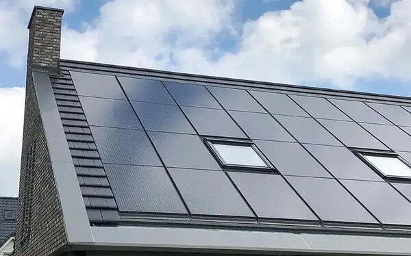 A house roof covered in dark solar panels integrated around two roof windows, next to a brick chimney