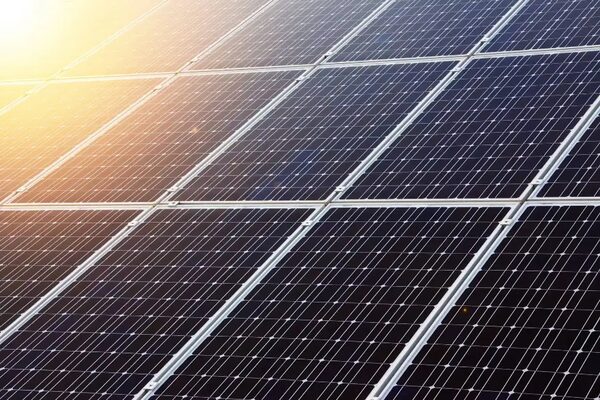 A close-up of solar panels on a roof with sunlight flaring across the top corner