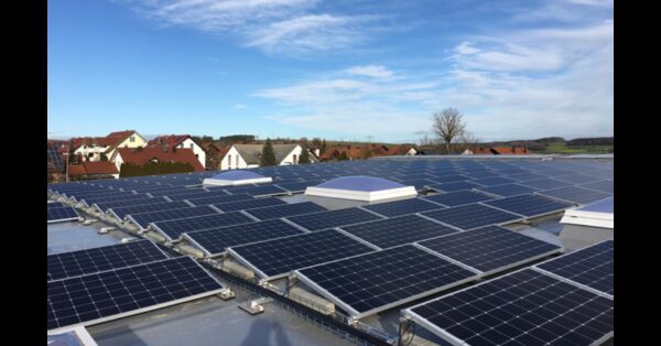 A large flat-roof solar panel array mounted at a low tilt angle, with rooftops of a village in the background
