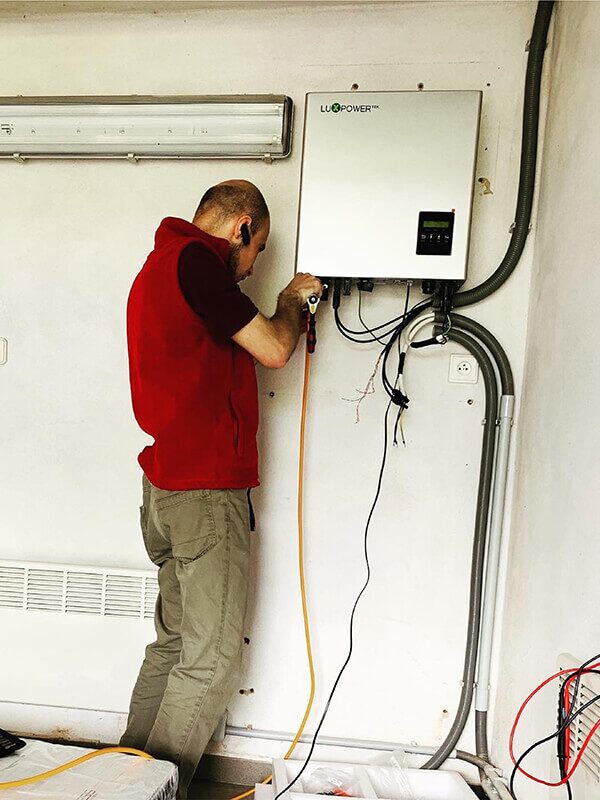 A technician installing a LuxPower wall-mounted solar inverter with cabling on a white wall
