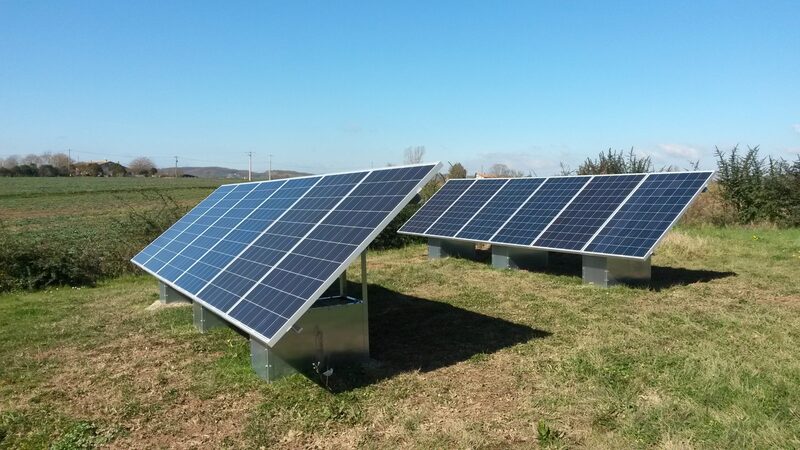 Two arrays of ground-mounted photovoltaic solar panels on metal frames in a grassy field