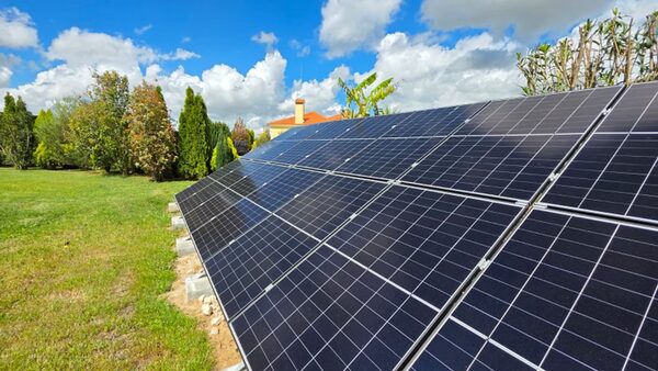 Ground-mounted solar panels on a grassy lawn with trees and a house in the background