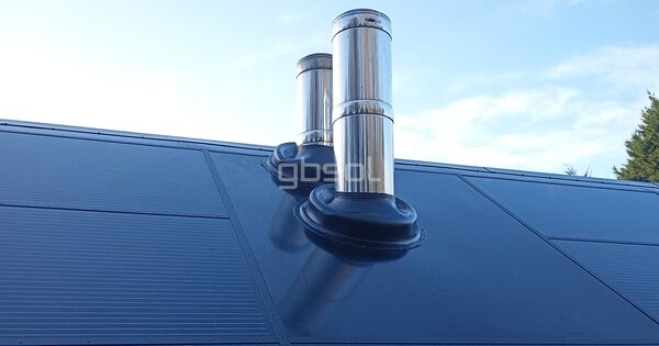 A roof fitted with dark in-roof solar panels around two stainless steel flue pipes sealed with black flashing boots