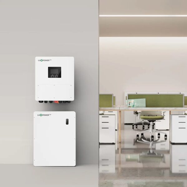 A white LuxpowerTek wall-mounted hybrid inverter and matching battery unit shown against a grey wall beside an office interior