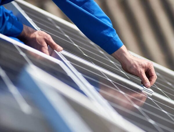 An installer in a blue work jacket positioning a solar panel on a roof