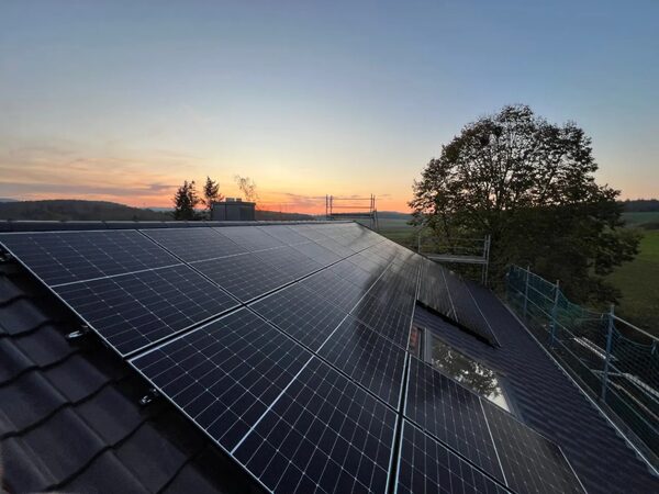 Solar panels installed on a tiled roof at sunset with countryside in the background