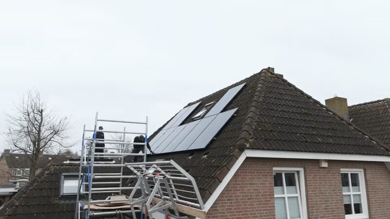 Installers on scaffolding fitting black solar panels on the tiled roof of a brick house
