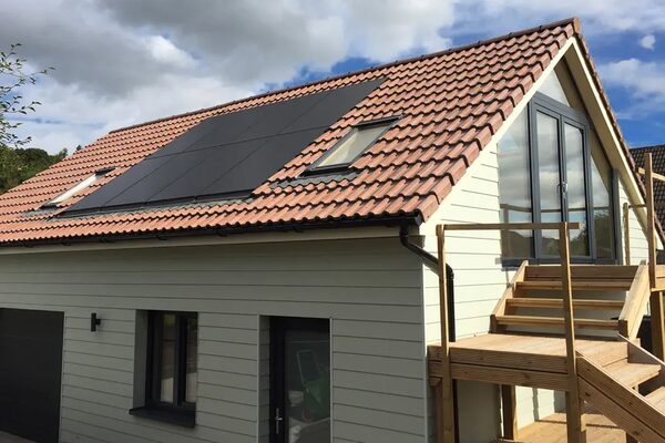 A modern house with a tiled roof fitted with black in-roof solar panels and roof windows