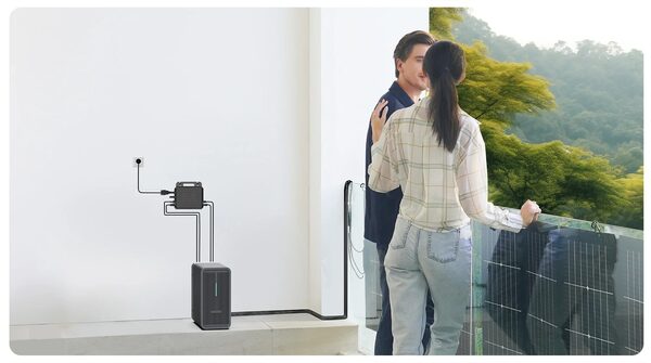 A couple on a balcony with a Marstek Saturn C balcony solar setup, a wall-mounted microinverter and a tall battery unit on the floor next to balcony solar panels