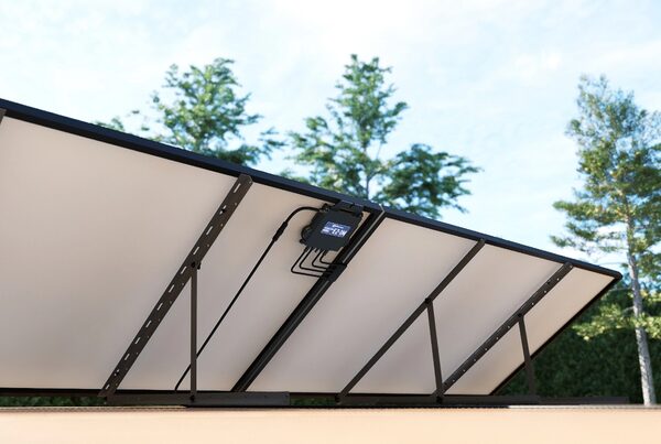 An APsystems EZ1 microinverter mounted on the underside of a row of solar panels on a ground or flat-roof mounting frame